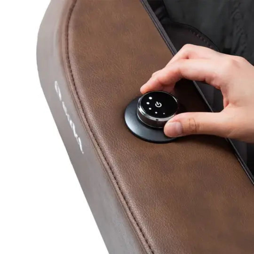 Hand pressing a control button on a brown massage chair.