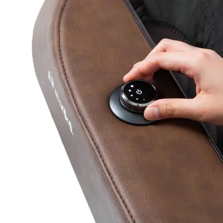 Hand pressing a control button on a brown massage chair.